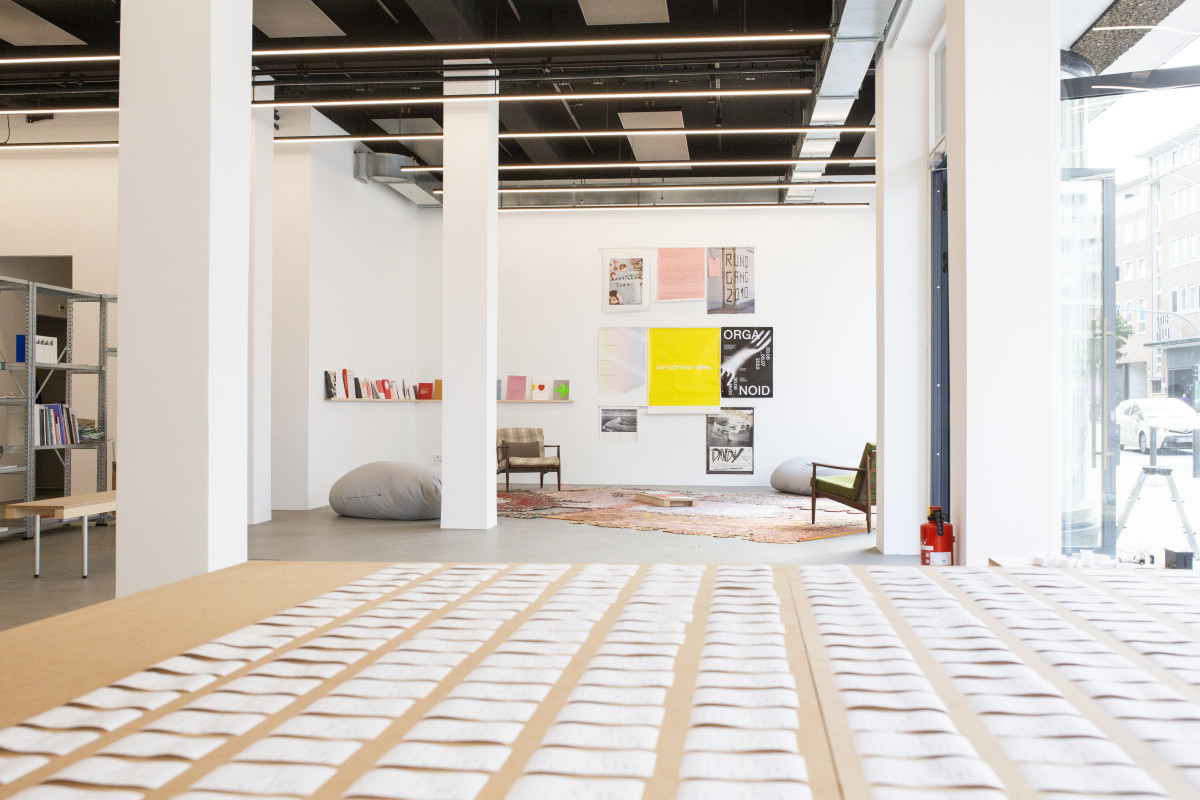 Einblick in den Raum mit dem Projekt von Jian Haake im Anschnitt und dem zentralen Fokus auf die Lese-Ecke mit Publikationen.