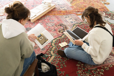 Zwei Frauen die Publikationen auf einem Teppich durchlesen