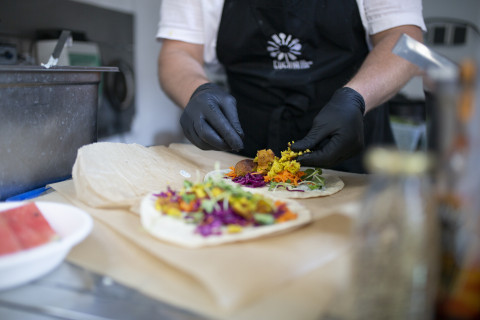 Mann im Foodtruck bereitet Falafelrolle zu.