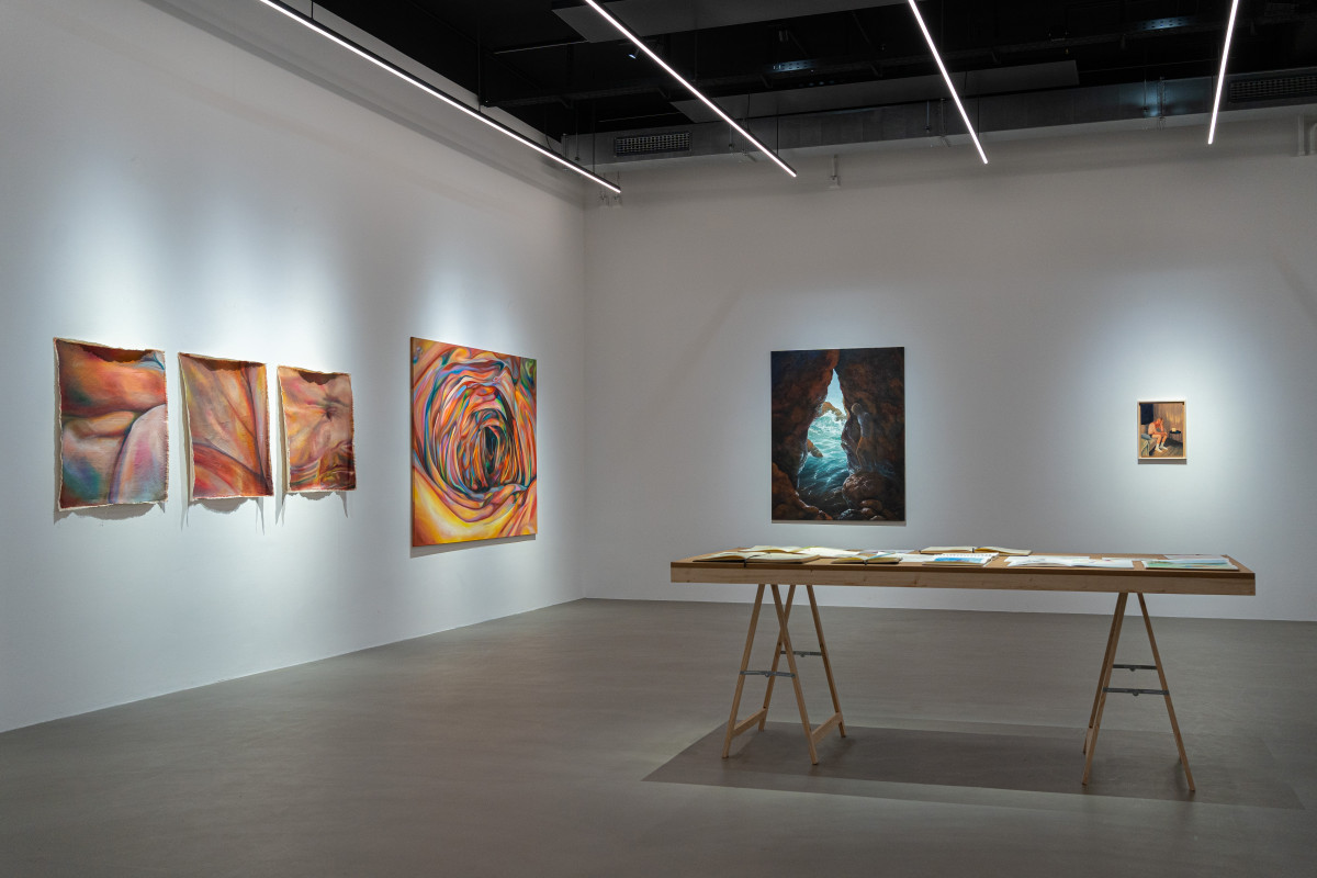 Raumansicht mit Arbeiten von Lisa Sophie Langhans auf der linken Wand und Arbeiten von Janna Schnoor an der Stirnseite des Raumes. Ein Tisch mit Skizzen von Janna Schnoor.