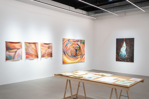 Raumansicht mit Arbeiten von Lisa Sophie Langhans auf der linken Wand und Arbeiten von Janna Schnoor an der Stirnseite des Raumes. Ein Tisch mit Skizzen von Janna Schnoor.